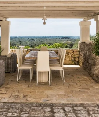 Terrazza coperta con lungo tavolo da pranzo e vista sugli ulivi, pavimento in pietra