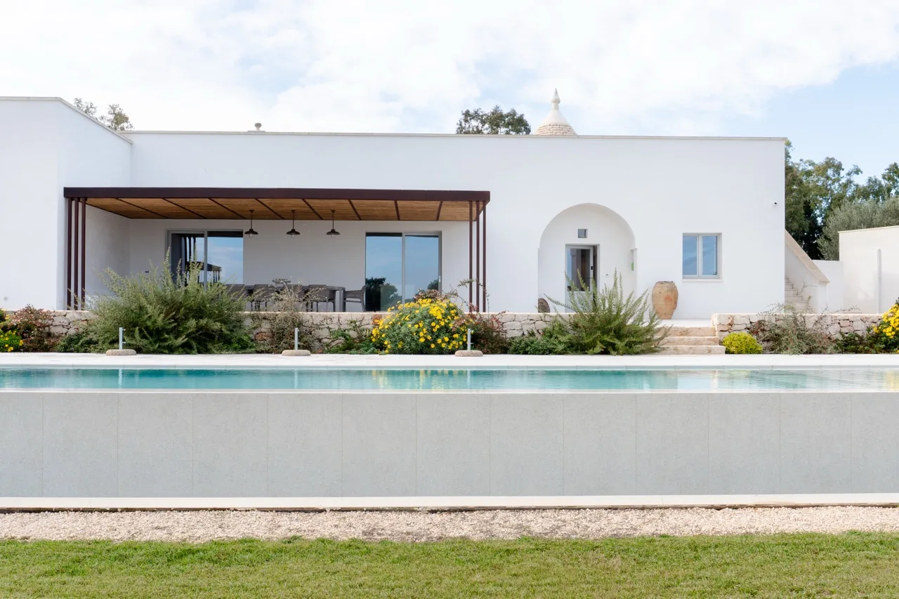 Outdoor Trani stone paving around a swimming pool, with the villa behind