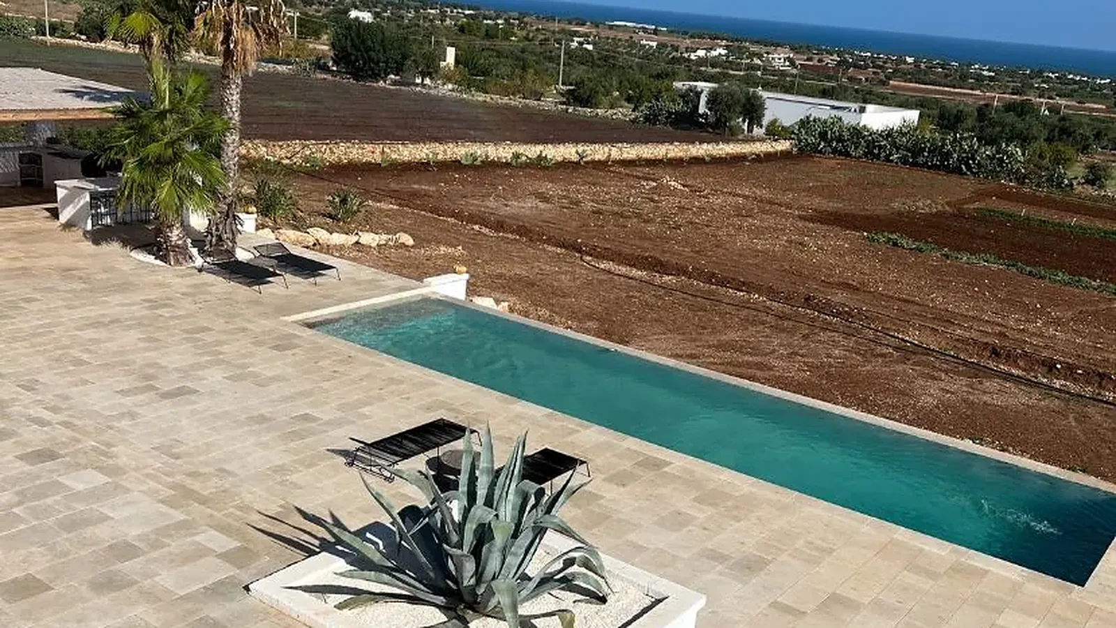 Terrasse en dalles de pierre au-dessus de la piscine, avec agave et campagne en fond