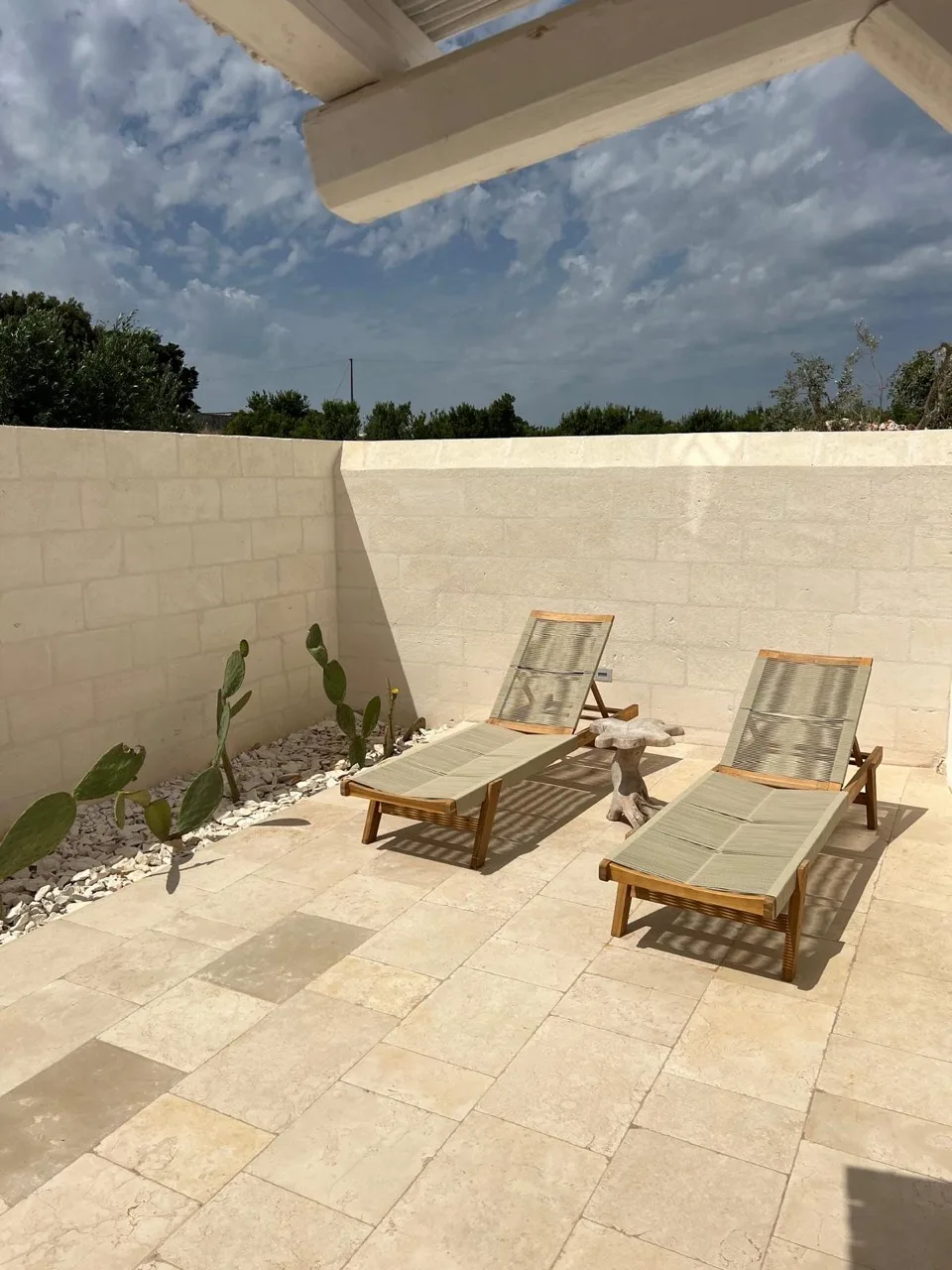 Outdoor patio paved in rustic Trani marble with sun loungers and a stone wall