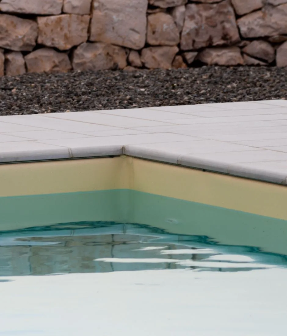 Bordo piscina in lastre di pietra chiara davanti a un muro in pietra a secco