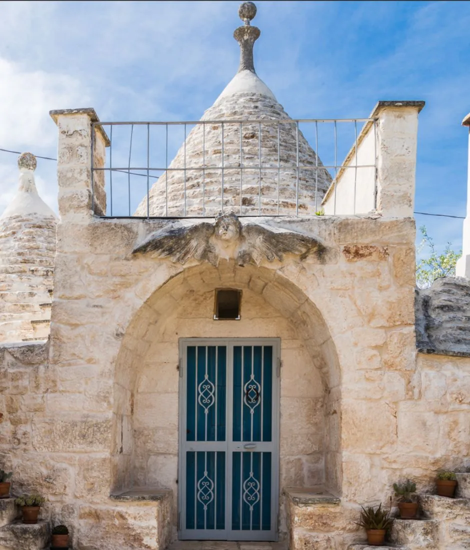 Façade of the restored trullo with a light blue door, stone steps and pots of succulents