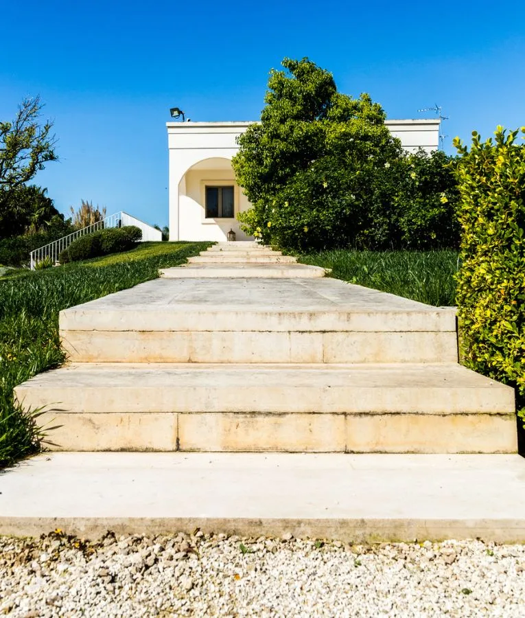 Ampia scalinata in pietra chiara che sale dal prato verso l'ingresso della villa