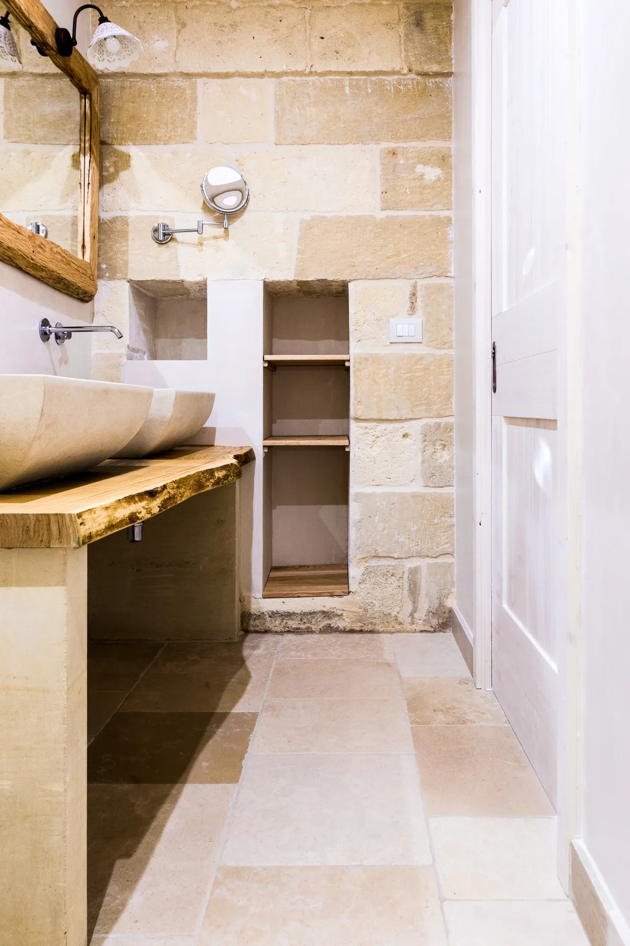 Bathroom at Masseria Longa with a stone basin on a wooden shelf and a floor in pale slabs