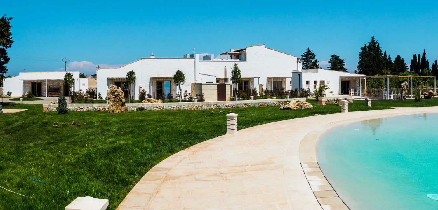 Esterno della masseria con prato, piscina e camminamento curvo in lastre di pietra chiara