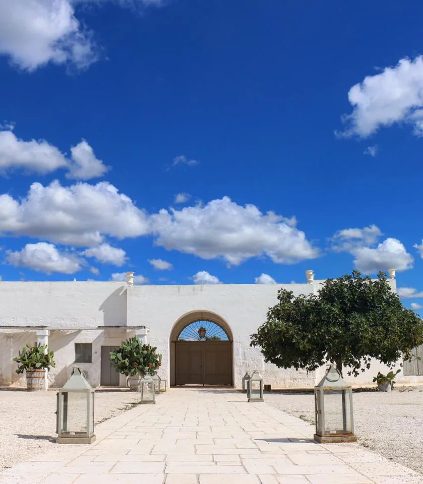 White façade of Masseria Potenti with an arched portal and a drive in stone slabs