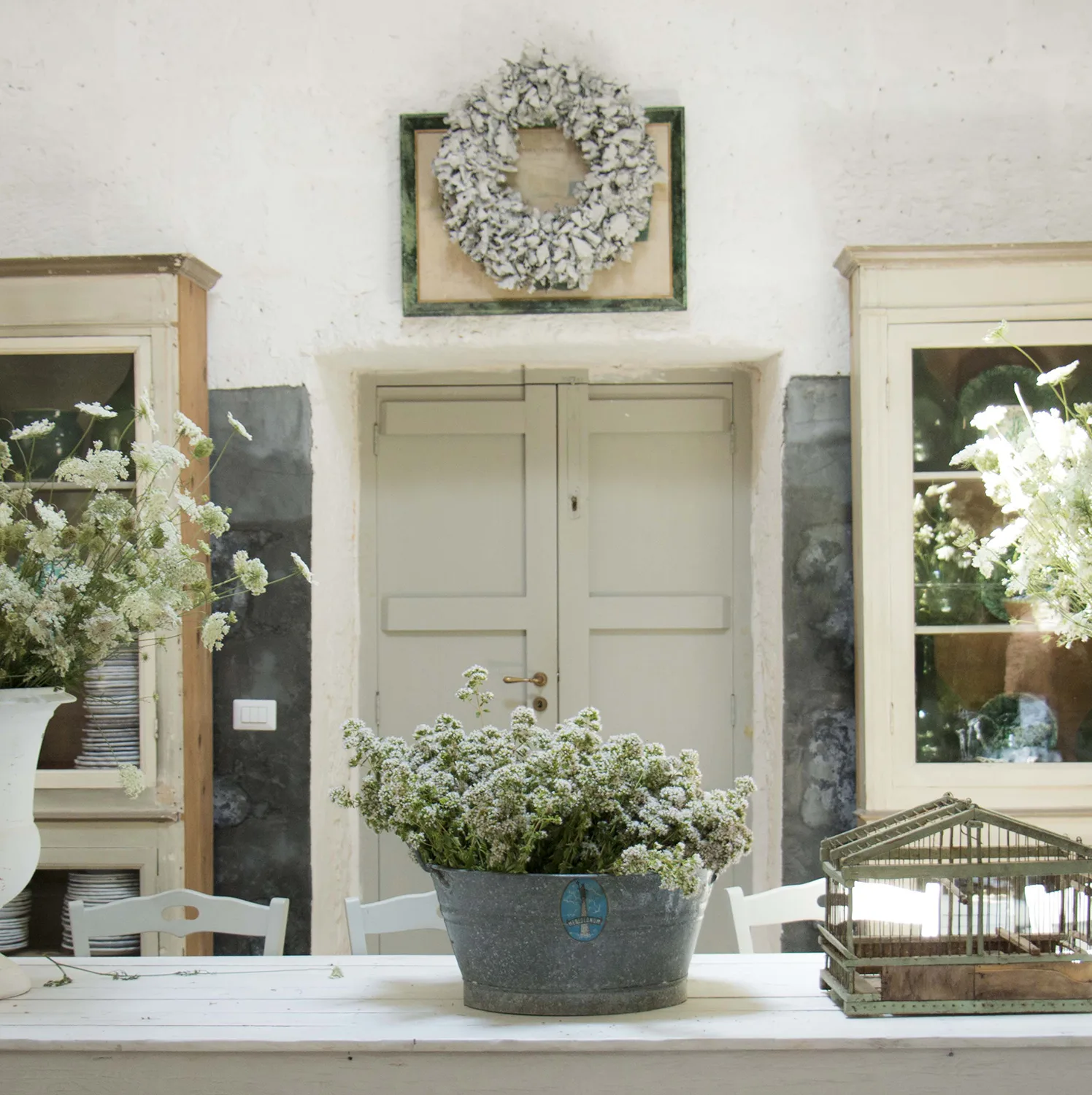 Sala da pranzo calcinata di bianco con credenze antiche e fiori di campo sul tavolo