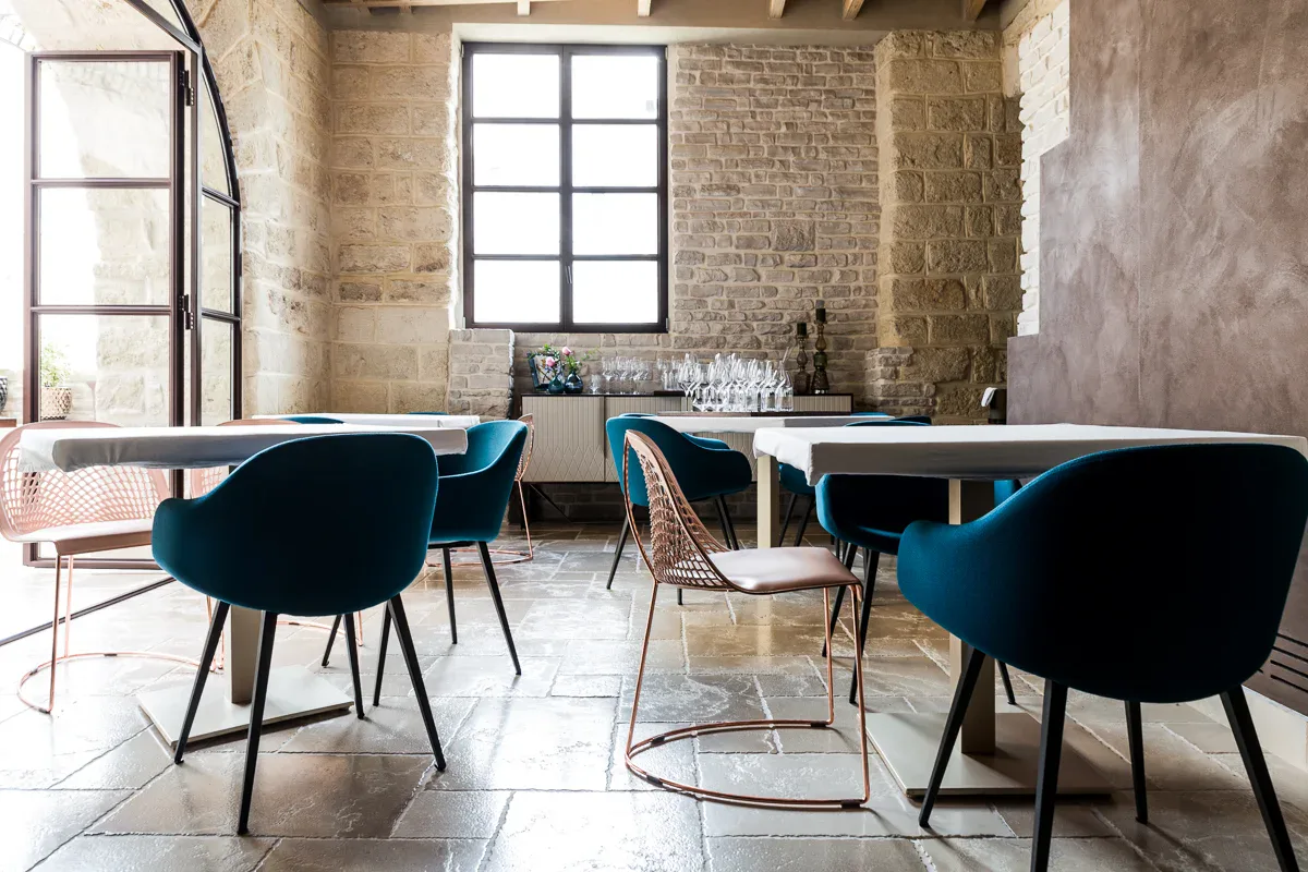 Dining room of the Quintessenza restaurant with blue chairs, walls in stone blocks and a floor in pale slabs